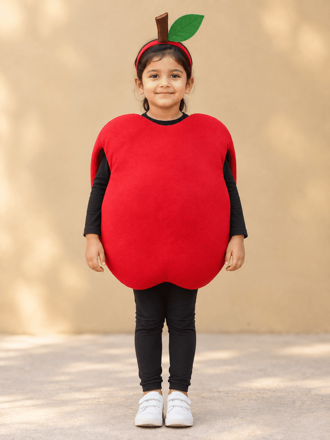 Young girl in a padded red apple tabard with a brown stalk and green leaf headband, worn over black sleeves and leggings